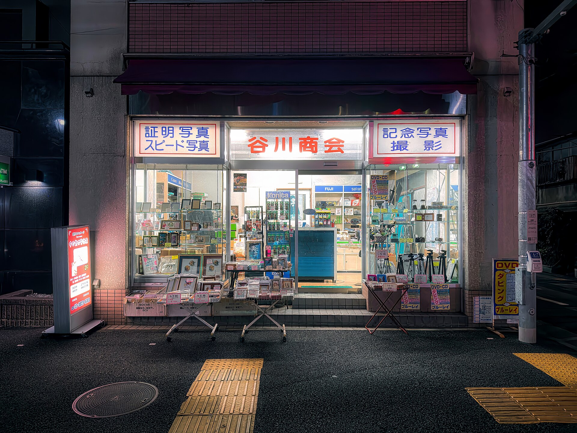 夜晚的东京根津，一家相机店的橱窗亮着灯，店内陈列着相机与冲印好的照片